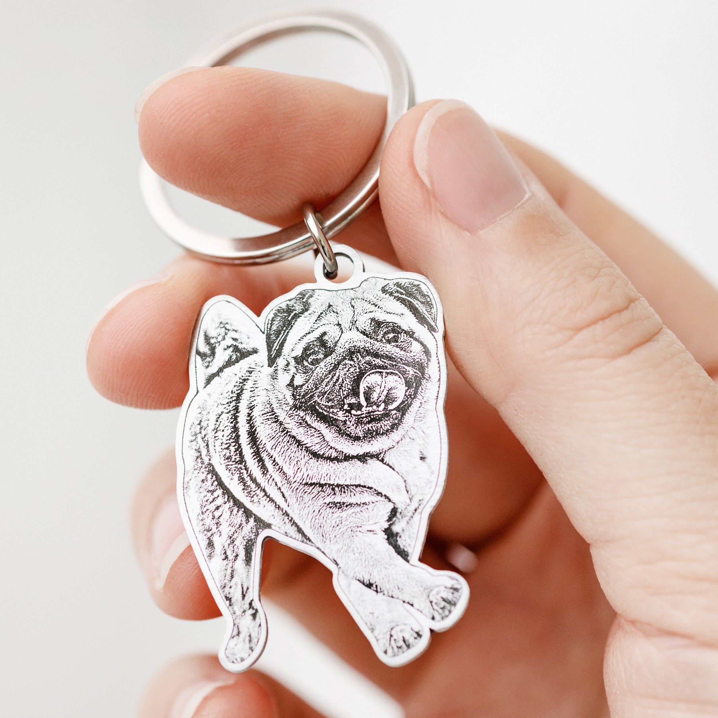 Silver custom dog photo keychain engraved with a pug, held in a hand